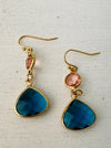 close-up of elegant gold drop earrings with pink crystal and deep blue teardrop stone.