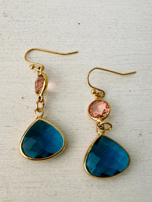 close-up of elegant gold drop earrings with pink crystal and deep blue teardrop stone.