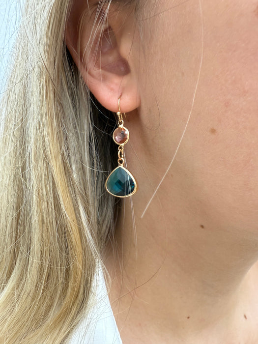 Elegant gold drop earrings with pink crystal and deep blue teardrop stone on a model
