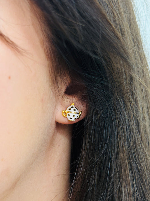 Close-up of an ear wearing a gold and black polka dot teacup earring.