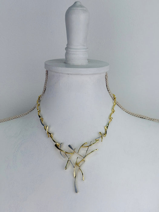 Gold and silver-tone abstract necklace with interwoven curved bars and adjustable chain on white background.