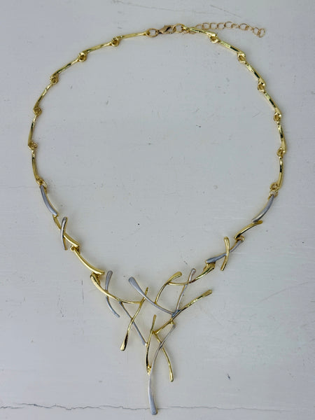 Gold and silver-tone abstract necklace with interwoven curved bars and adjustable chain on white background.