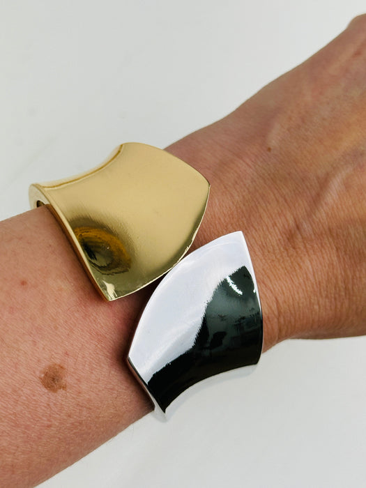 Gold and silver tone cuff bracelet with sculptural leaf shape and polished finish displayed on a model.