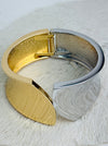 Gold and silver tone cuff bracelet with sculptural leaf shape and polished finish on a white background.