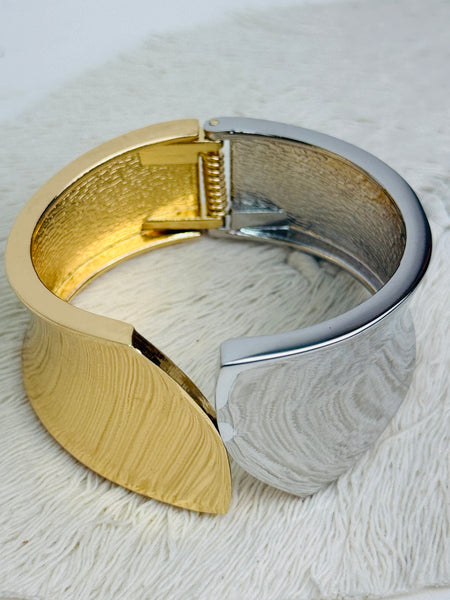 Gold and silver tone cuff bracelet with sculptural leaf shape and polished finish on a white background.