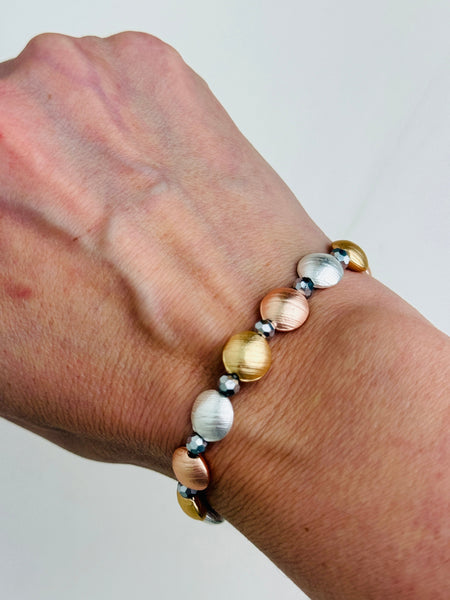 Tri-tone metallic beaded elastic bracelet in gold, silver and rose gold tones with grey spacer beads, displayed on a model.