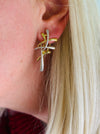 Close-up of a model wearing gold and silver tone abstract earrings with interwoven curved bars.
