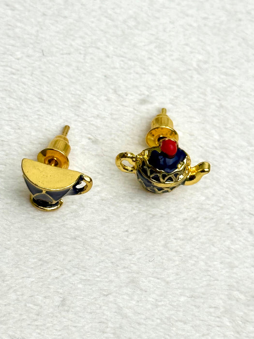 Pair of earrings shaped like teapots on a white fabric background