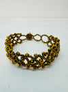 A gold-coloured bracelet with a geometric pattern and seed bead detailing.