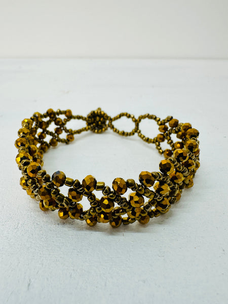 A gold-coloured bracelet with a geometric pattern and seed bead detailing.