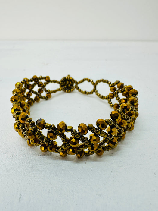 A gold-coloured bracelet with a geometric pattern and seed bead detailing.