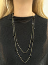 Long necklace with black square pendants on a person wearing a black top.