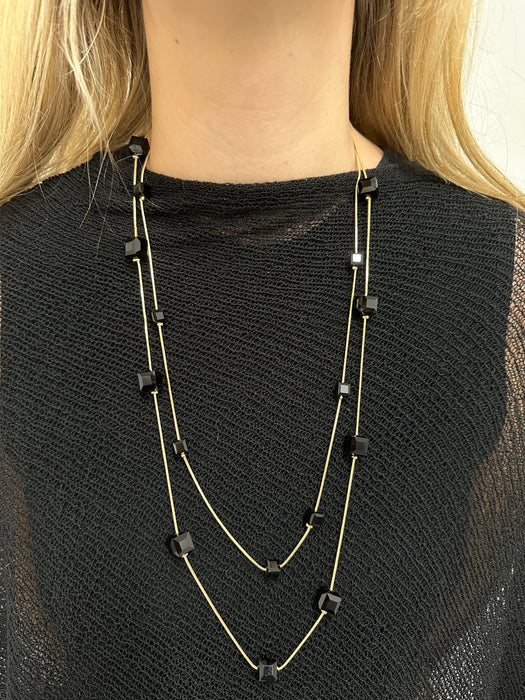 Long necklace with black square pendants on a person wearing a black top.