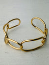 Modern gold-tone cuff bracelet with open link design, displayed on a table.