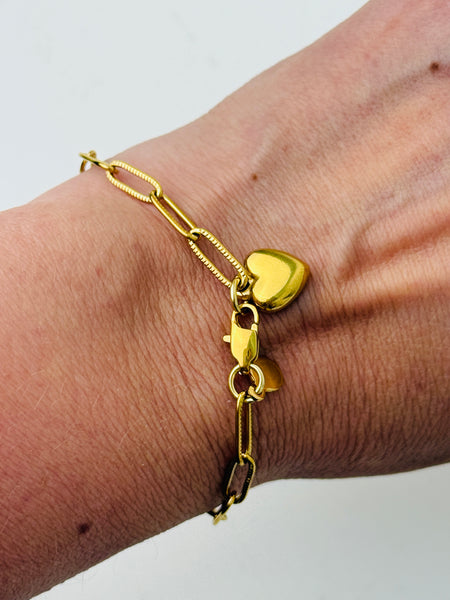 Gold-tone link chain bracelet with polished heart charm, displayed on a model.