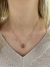 A gold necklace with a double heart pendant featuring a crystal detail, worn by a person with a beige knit sweater.