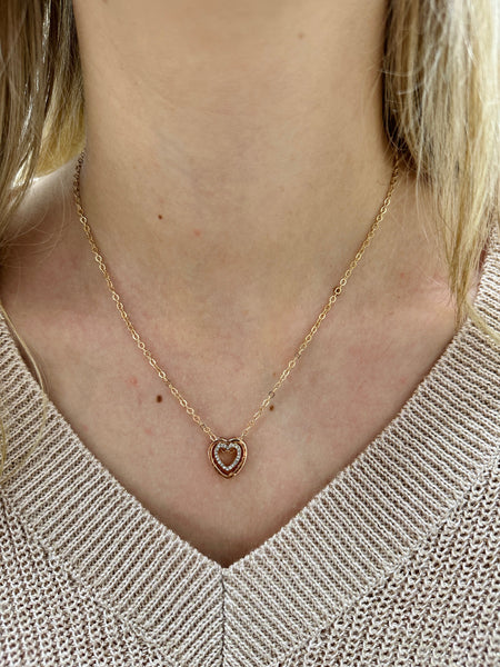 A gold necklace with a double heart pendant featuring a crystal detail, worn by a person with a beige knit sweater.