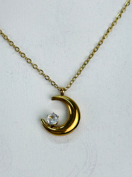 Gold crescent moon necklace with a diamond on a white background