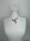 Rose gold floral necklace with enamel flowers in soft pink, deep rose and pearl tones, and small pink crystal accents on brach style design, displayed on a mannequin.