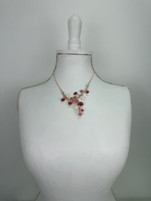 Rose gold floral necklace with enamel flowers in soft pink, deep rose and pearl tones, and small pink crystal accents on brach style design, displayed on a mannequin.