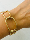 Modern gold-tone cuff bracelet with open link design, displayed on a model.