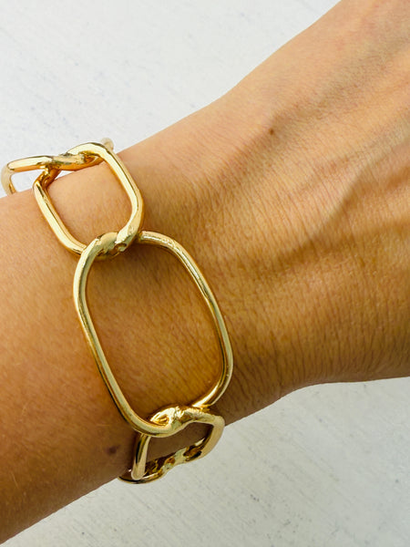 Modern gold-tone cuff bracelet with open link design, displayed on a model.