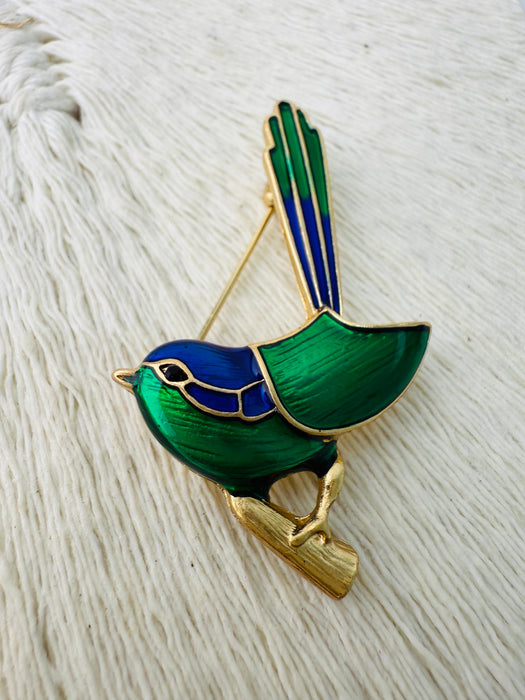 Bird-shaped brooch with green and blue design on a textured white background