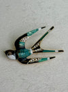 close-up of enamel bird brooch with green and brown  feathers on a gray background