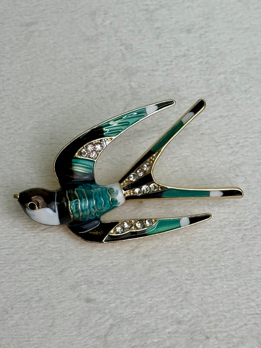 close-up of enamel bird brooch with green and brown  feathers on a gray background