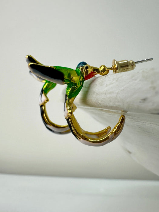 A pair of hummingbird-shaped earrings with green and gold colors on a white surface.