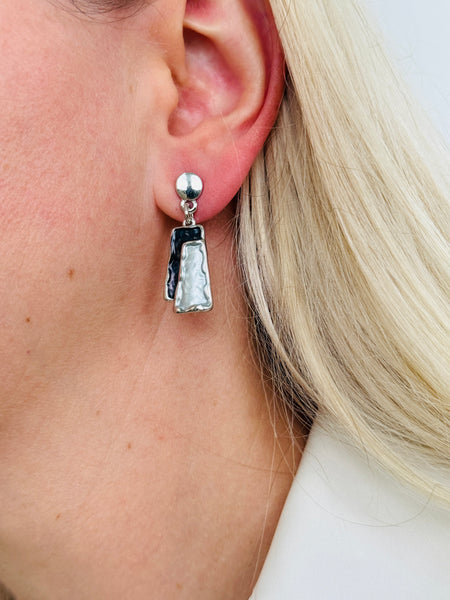 Grey and gunmetal rectangular enamel drop earrings with silver-tone outline, displayed on a model.