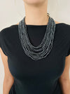 A person wearing a black top and showcasing a gunmetal seed bead necklace with multiple strands and a hand-carved wooden buckle.