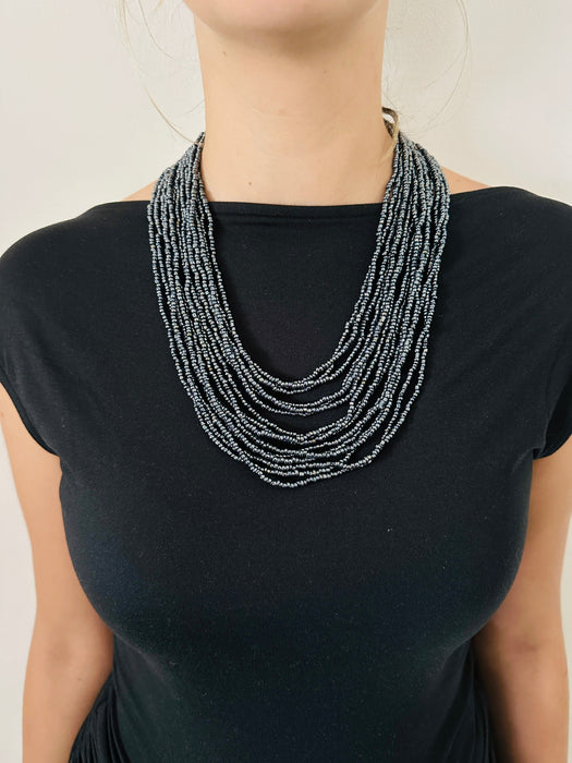 A person wearing a black top and showcasing a gunmetal seed bead necklace with multiple strands and a hand-carved wooden buckle.