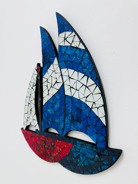 side angle of mosaic sailboat wall art with blue, white, and red colors on a white background