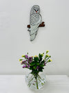 A handmade and hand painted mosaic glass owl mounted on a wall above a vase with flowers.