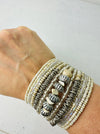 close-up of beaded bracelets with a mix of white, beige, and metallic colours, featuring various designs and materials.