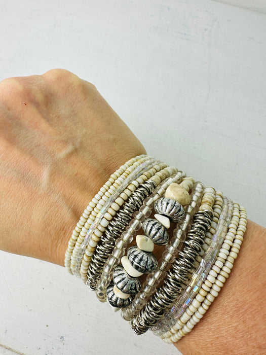 close-up of beaded bracelets with a mix of white, beige, and metallic colours, featuring various designs and materials.