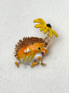 Hedgehog-shaped brooch with a yellow flower on a white background
