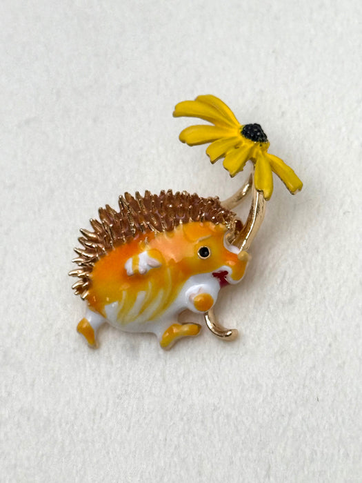 Hedgehog-shaped brooch with a yellow flower on a white background