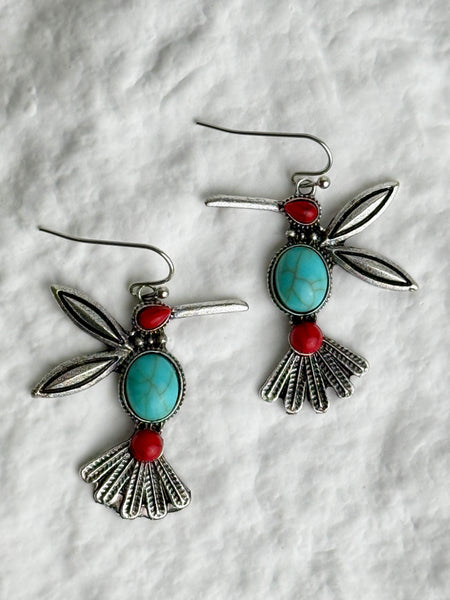 Pair of silver earrings with turquoise and red stones on a textured white background