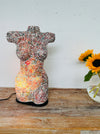 front view of glass mosaic bust lamp in burgundy colours with light on stood on wooden surface next to a vase of sunflowers