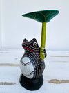 side view of wooden frog holding a leaf as an umbrella