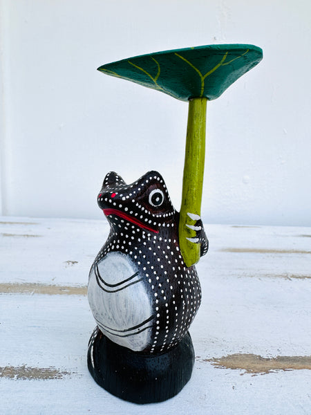 side view of wooden frog holding a leaf as an umbrella