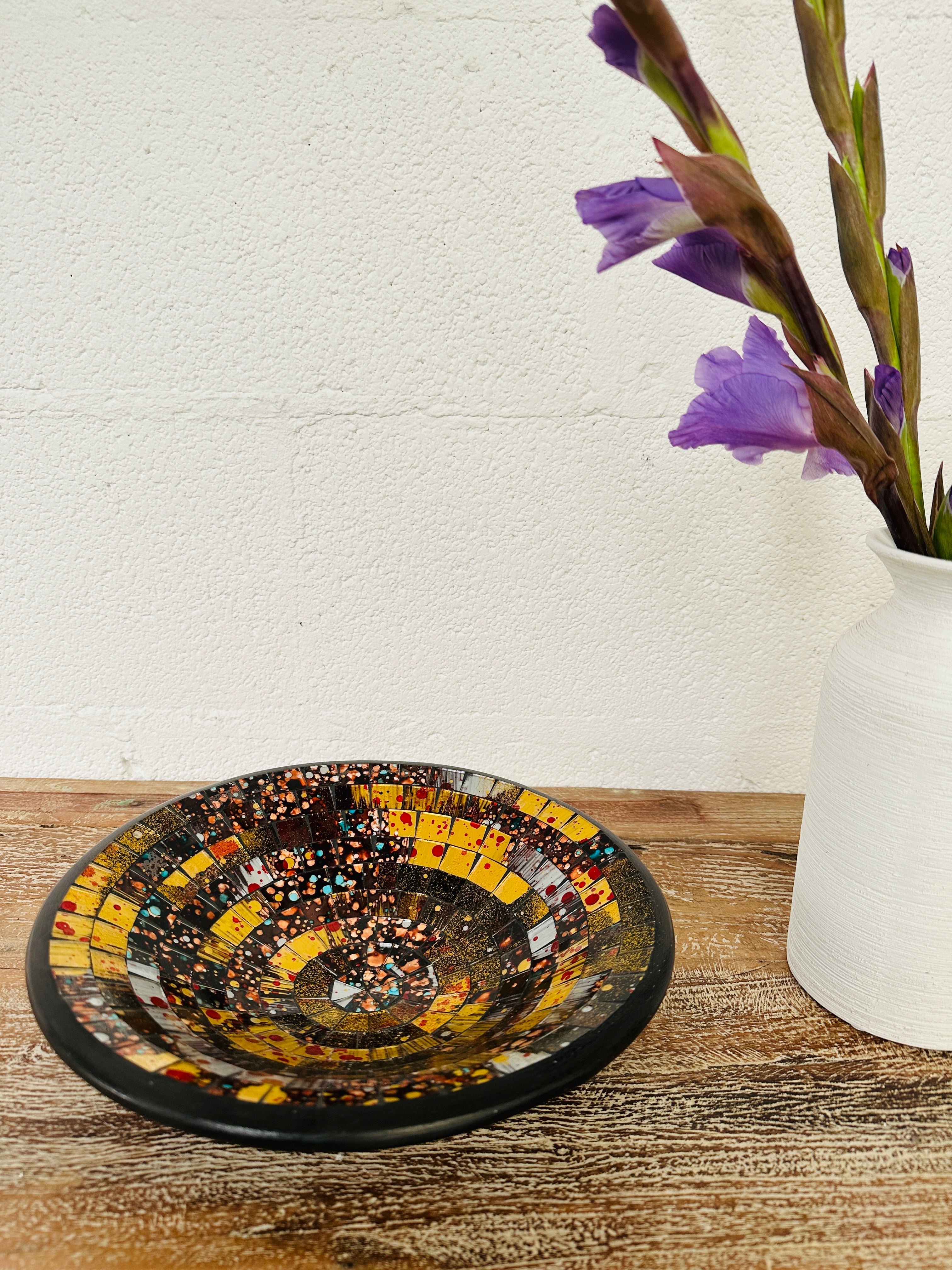 display view of mosaic bowl next to a vase of flowers on a table