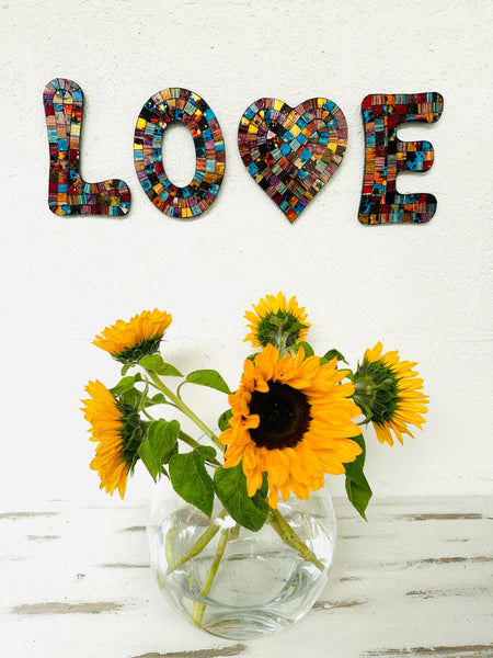 display view of mosaic love on the wall with a vase of sunflowers below