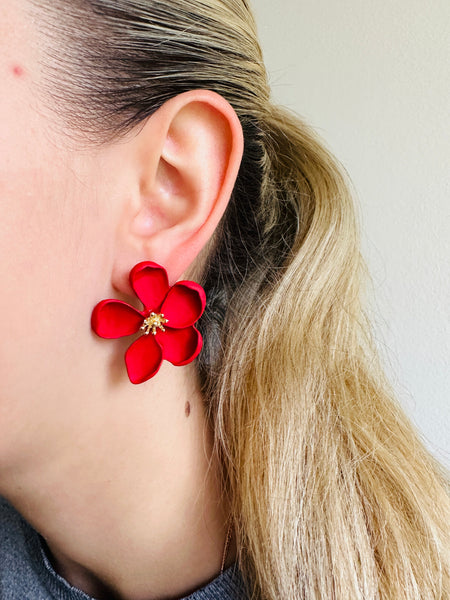 front view of matte red flower-shaped earring worn by a person 