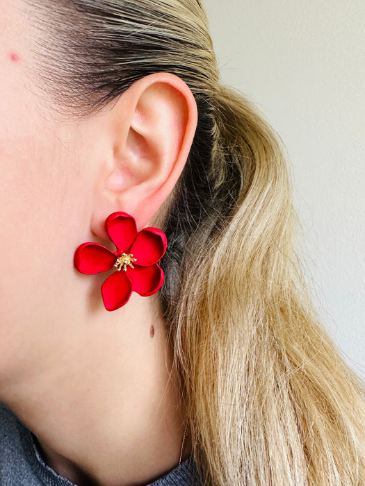 front view of matte red flower-shaped earring worn by a person 