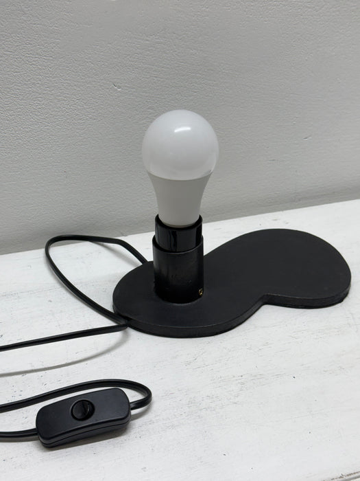 a black swivel socket holding a frosted white bulb, and a black power cord with a switch, set against a light gray wall and white surface.