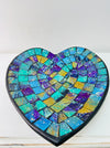 Top view of handmade mosaic heart bowl in blue, green and turquoise glass pieces on white background.