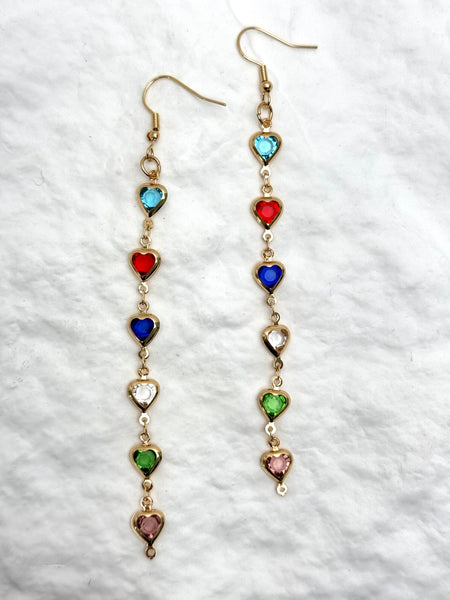 Long earrings with heart-shaped gemstones on a textured white background